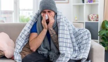 young-ill-man-wearing-scarf-winter-hat-wrapped-blanket-sitting-sofa-living-room-wiping-nose-with-napkin-with-closed-eyes.jpg